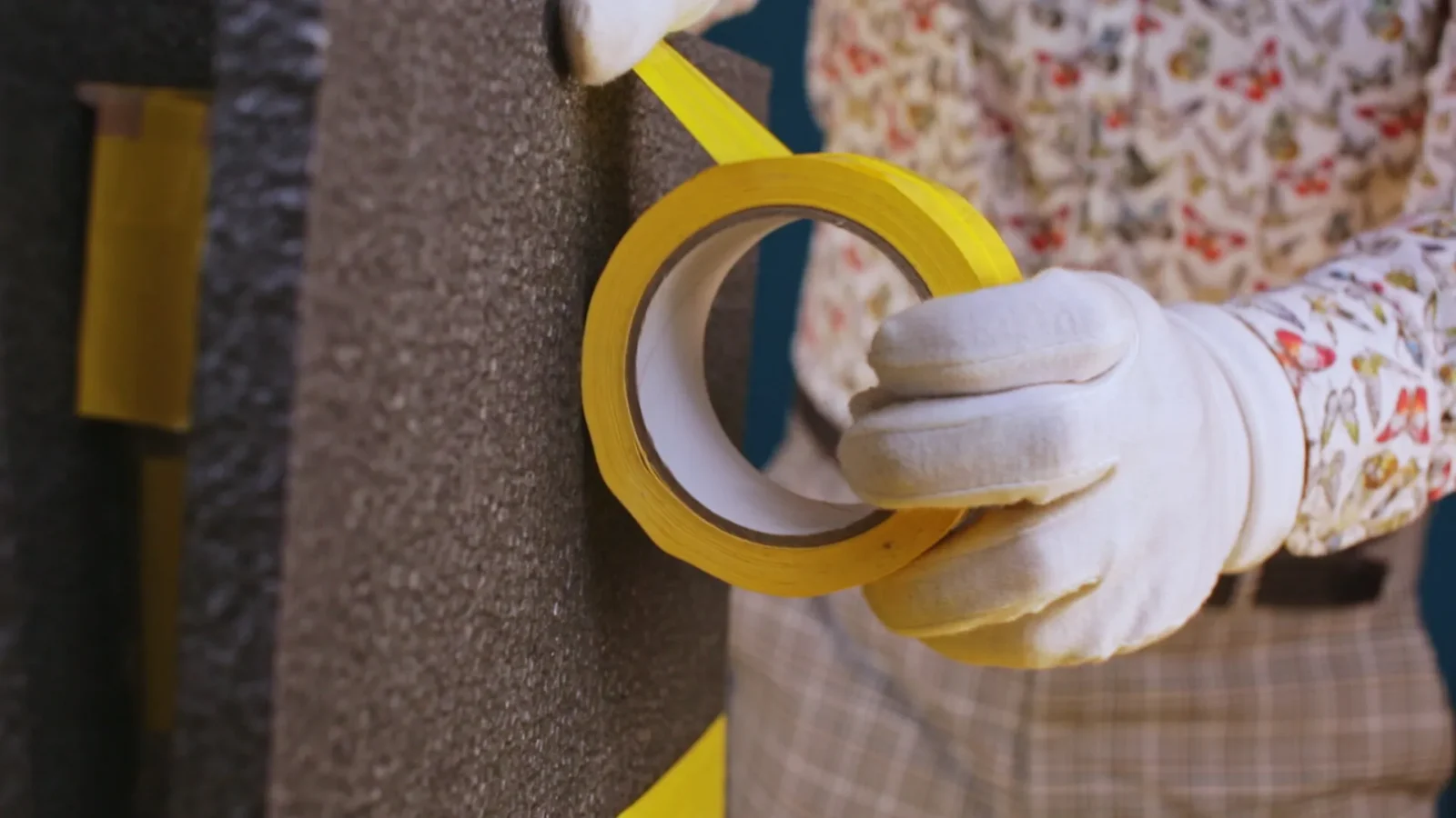 White-gloved hands holding yellow packing tape beside protective foam.